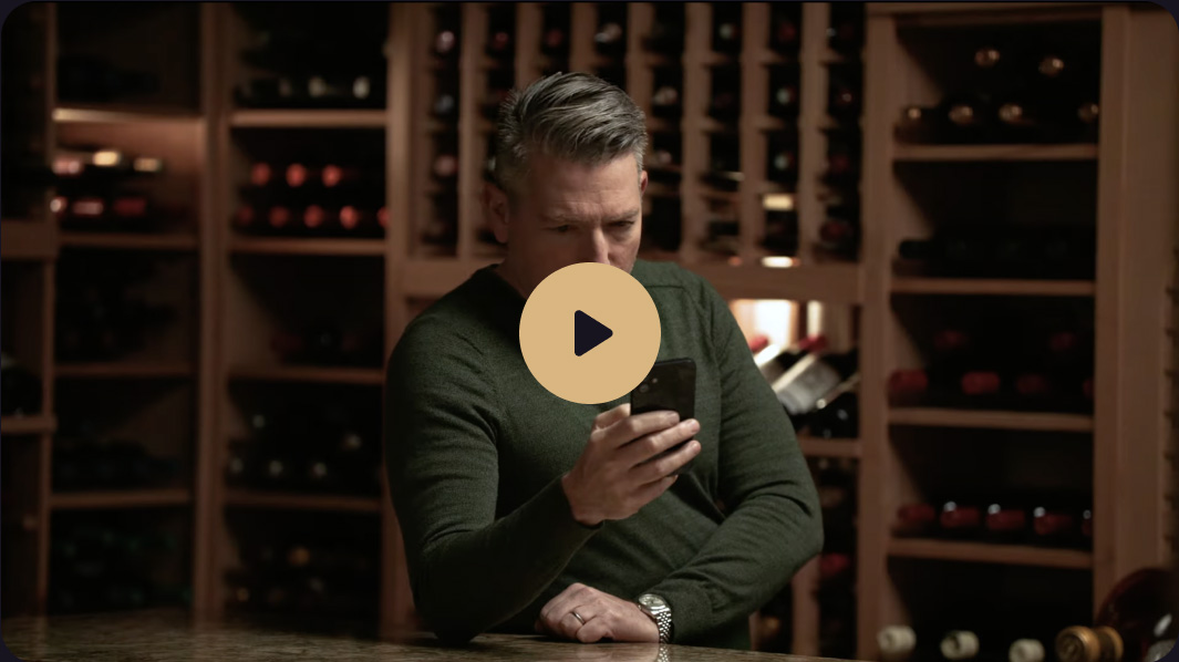 Sophisticated man intently views his mobile app while standing in front of a wine cellar.